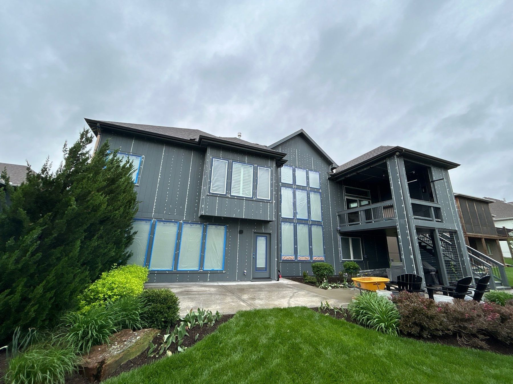 Exterior prep — windows and fixtures fully masked before spraying, with caulked seams visible across the siding